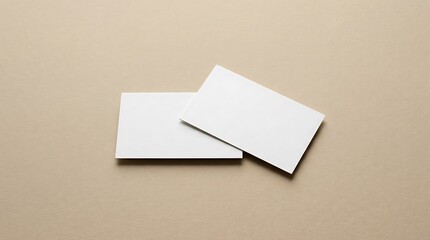 Fototapeta premium Two overlapping clean white rectangular business cards lying diagonally on solid soft beige background for professional branding showcase.