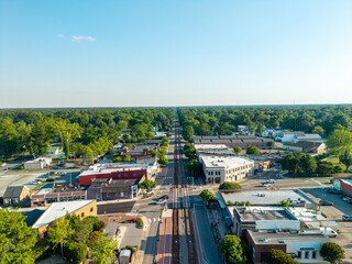 Ashland, Virginia, aerial view looking straight down the historic train tracks running through the center of the downtown district lined with small businesses, trees, and roads. © Eli