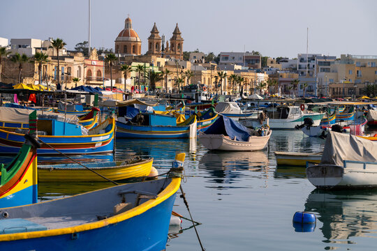 Traditional Maltese fishing boats moored in Marsaxlokk harbor with the Parish Church of Our Lady of Pompei in background, Malta.
