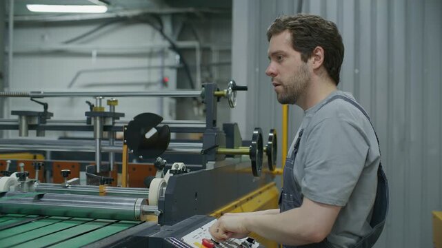 Skilled printing press operator manually calibrating machinery using handwheel and adjusting settings on control console while monitoring production process in industrial print shop