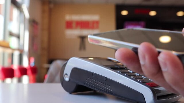 Customer using smartphone for contactless payment with nfc technology on a pos terminal in a restaurant, a close up view of the tap to pay transaction process