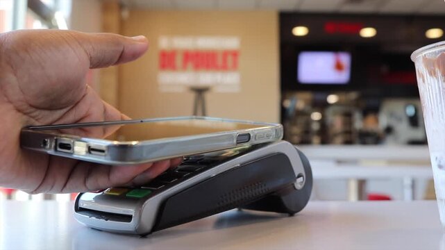 Customer's hand making contactless mobile payment using a smartphone on a pos terminal in a restaurant, illustrating modern secure e commerce and nfc technology