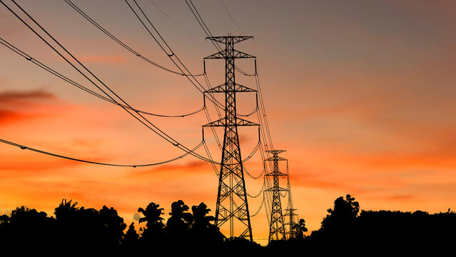 Silhouettes of electrical pylons stand against a vibrant sunset sky, with power lines stretching across the frame