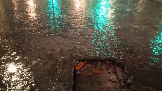 Reflections of urban lights on a soaked street on a rainy night with a visible manhole cover