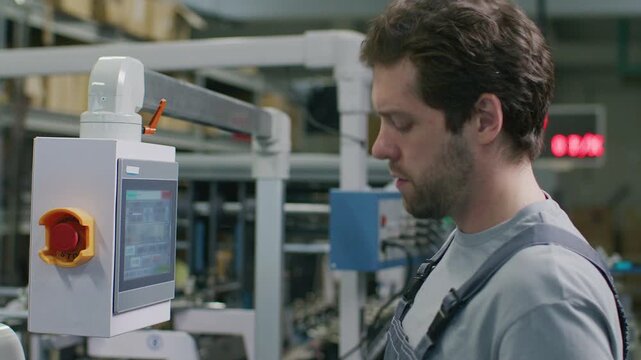 Male technician in overalls using digital touchscreen control panel to operate automated industrial printing machine in modern commercial print shop