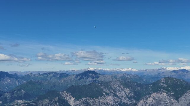 Paraglider soaring above Monte Baldo landscape with lake Garda, panoramic mountain vistas, adventure sport, freedom, travel photography, aerial view