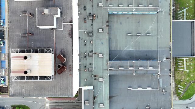 Aerial view of industrial enterprise rooftops showcasing interconnected structures, ventilation systems, and smoke emissions, highlighting the complexity of industrial architecture and operational ele