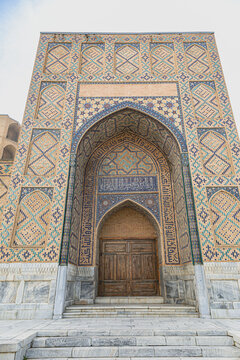 Grand tiled side portal and entrance of the historic Bibi Khanym Mosque featuring complex Islamic blue mosaics under a cloudy sky in Samarkand, Uzbekistan.