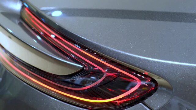 LED tail lamp cluster detail glowing on silver metallic rear bodywork. Dramatic red light signature of British luxury supercar design for premium automotive editorial content.