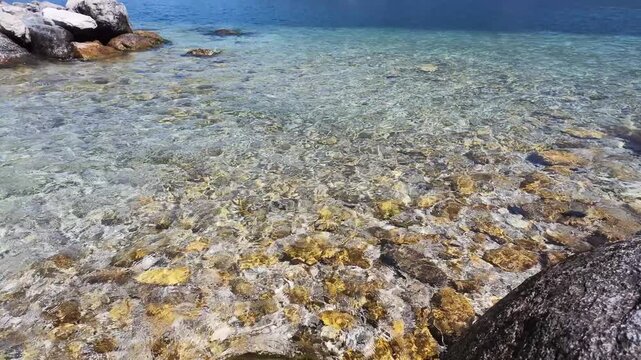 Clear turquoise water surface over golden pebbles at lake shore, rippling texture, serene travel background