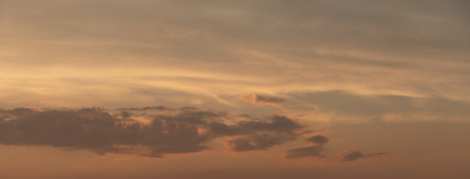 Gentle pastel sunset sky with layered clouds in warm peach golden hues, calm atmospheric natural background
