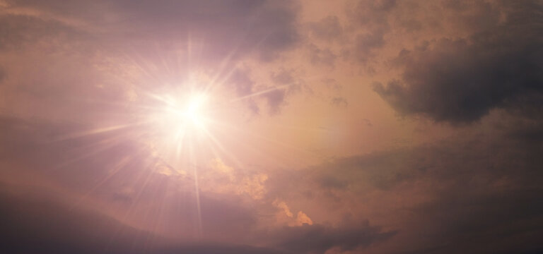 Bright sun with light rays breaking through dramatic clouds in warm pink purple tones, majestic celestial landscape