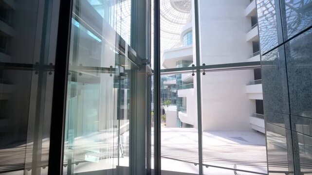 Tracking shot through glass atrium revealing modern building courtyard with skylight from interior corridor