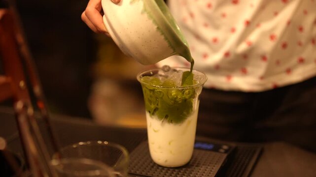 Preparing Japanese Matcha Green Tea, green tea milk cup drink iced drink layered drink beverage pouring barista cafe clear glass hand preparing creamy cold refreshment food preparation counter