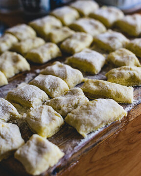 Close-up of raw potato dumplings covered in flour on a wooden pastry board, traditional Polish kopytka or Italian gnocchi preparation, culinary food concept background