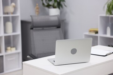Fototapeta premium White desk with laptop, clipboard, chair and decor in office, closeup