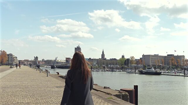 Woman walking by marina in Dunkirk France on sunny spring day