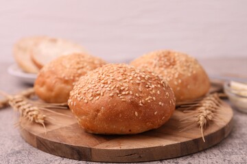 Fototapeta premium Yummy buns with sesame seeds and wheat ears on grey table, closeup