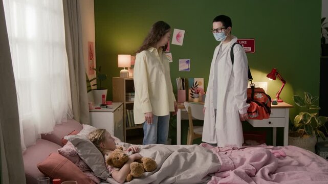 Woman leading female doctor into room and pointing at sick daughter, physician sitting down on bed and starting conversation with girl and her mother