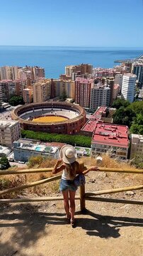 high angle view of a female tourist looking at plaza de toros and malaga city panorama from gibralfaro viewpoint, spain