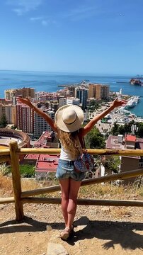 happy female tourist with arms raised looking at malaga city panorama plaza de toros and port from gibralfaro viewpoint spain