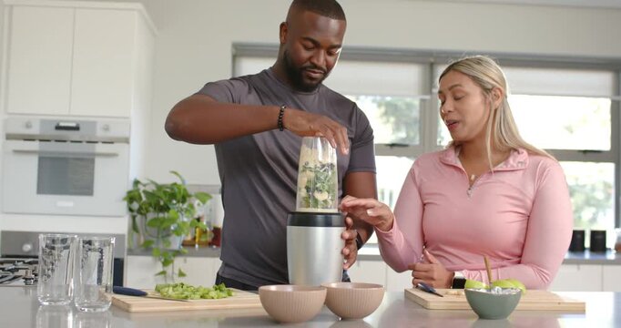 Couple at kitchen island man placing blender cup pressing base woman pointing making green smoothie