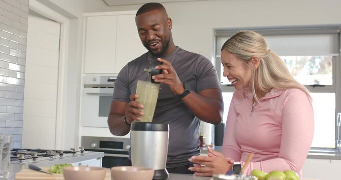 Diverse couple making green smoothie in home kitchen man holding jar tightening lid, woman laughing