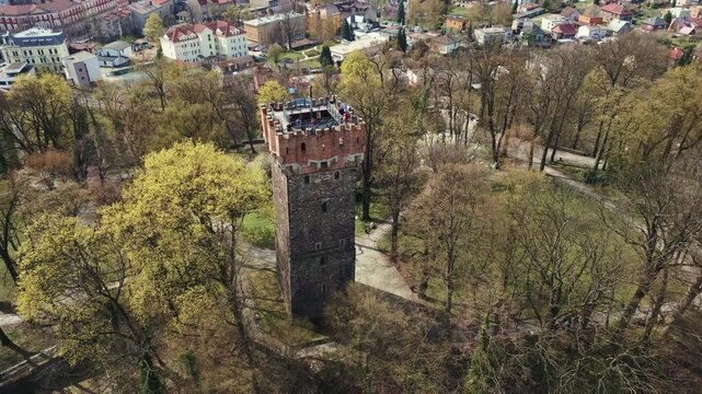 Aerial pull back and ascend from the historic Piast Tower in Cieszyn, Poland. Tourists look out from the stone observation deck on a sunny day.
