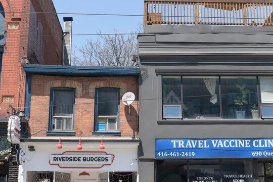 exterior building facades and signs of Riverside Burgers (688 Queen St E) and Travel Vaccine Clinic (690 Queen St E), Toronto