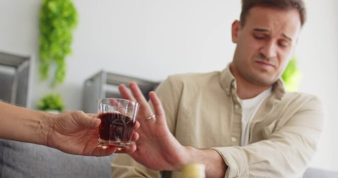 Man shows refusal to alcohol for sobriety. At home, he rejects the beverage, prioritizing health, recovery, and abstinence amid social pressure. Message: choose health over harmful drinking.