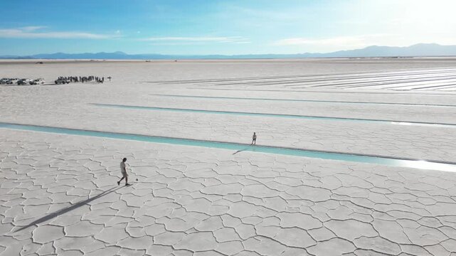 Man and child playing soccer beside turquoise saltwater pools on the salt flats of Salinas Grandes, Jujuy, Argentina