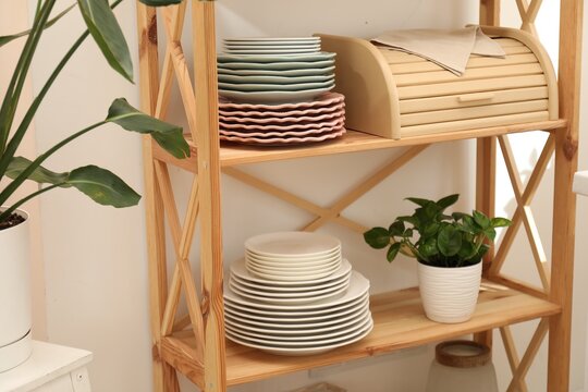Set of clean plates, breadbox and houseplant on wooden shelves in kitchen