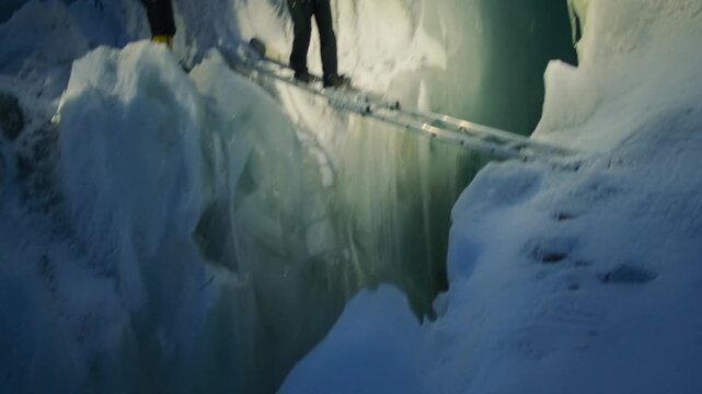 Two climbers with headlamps carefully crossing a dangerous glacial crevasse on a ladder