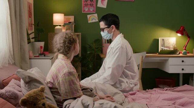 Middle-aged female doctor with short hair checking throat of teenage girl using disposable tongue depressor during home visit