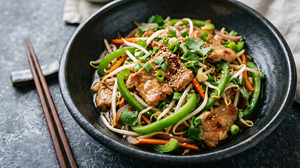 Fototapeta premium Stir-fried chicken with green beans and noodles in black bowl on dark table with chopsticks