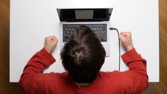 Young man overwhelmed by work, slamming his forehead on a laptop at a white desk in a home office, showing stress, frustration, burnout and technology related despair and exhaustion