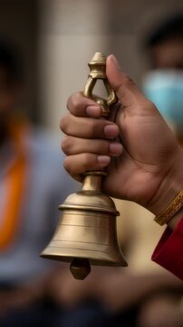 Woman holding copper hand bell for ritual. Devotee gripping traditional prayer instrument during religious ceremony. Hindu worship practice during Ganesh Chaturthi. Vertical video