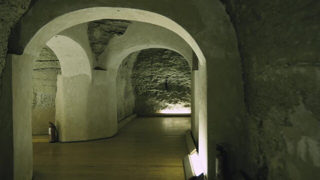 Dark underground corridor with stone arches leading to massive granite sarcophagus inside Serapeum of Saqqara, Egypt, dramatic warm lighting on ancient rock-cut tunnel walls.