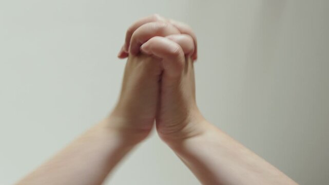 Hands with interlaced fingers locked actively touch thenar area. Sound with clapping during exercise with hands and palms, upward shot, white background.
