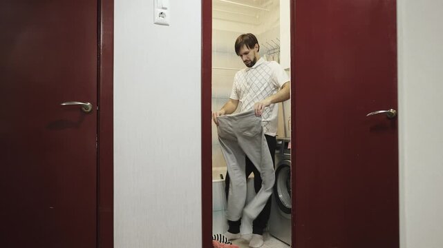 Caucasian man shakes pants in bathroom after washing. Lonely bachelor doing household chores.