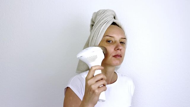 Woman using handheld photo rejuvenation laser machine near cheek for professional home skincare. Modern dermatology and beauty therapy technology