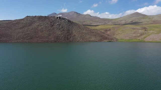 This stunning aerial drone shot captures the serene beauty of a high-altitude alpine lake nestled against majestic mountain peaks under a clear blue sky on a summer day.

