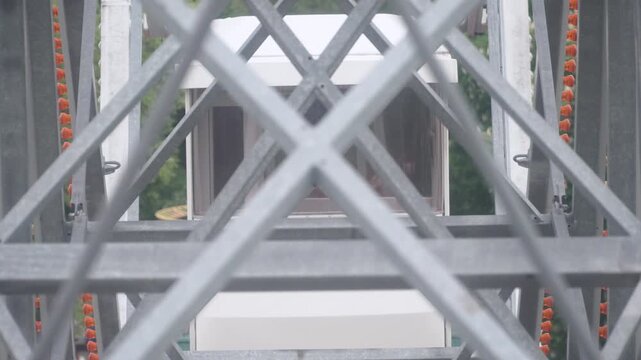 Lifting cabin of Ferris wheel attraction with view through metal frame of parallel cabin. Rotation and lifting of Ferris wheel in amusement park.