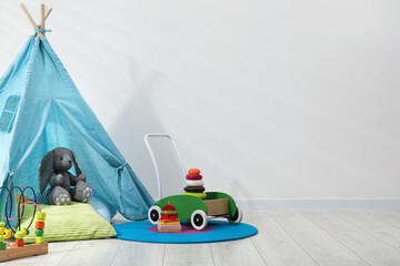 Wigwam, toys and pillows near white wall in child's room, closeup. Space for text © New Africa
