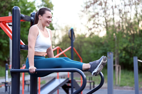 Athletic woman exercising on parallel bars at outdoor gym. Space for text