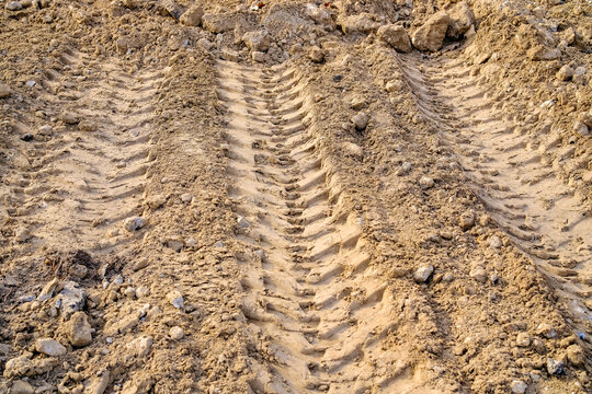 Heavy machinery tire tracks on dry clay soil at construction site with rough textured ground and excavated earth