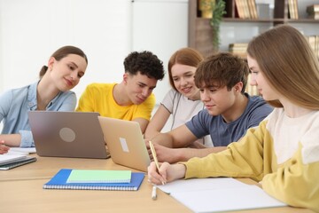 Fototapeta premium Group of students studying with laptops and notebooks at wooden desk in classroom