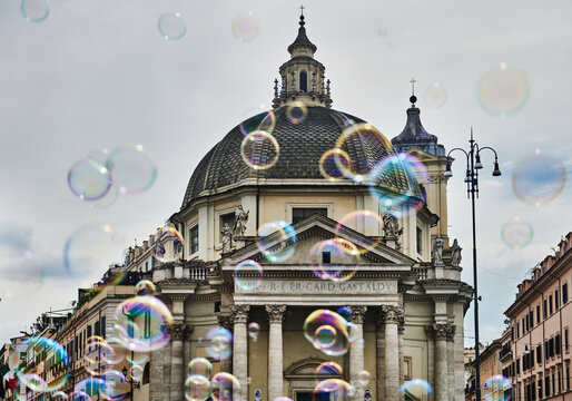 a playful cloud of soap bubbles floating in front of Chiesa Santa Maria dei Miracoli (17th century), located in the iconic Piazza del Popolo in Rome, Italy, Europe 