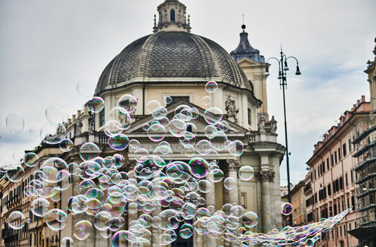 a playful cloud of soap bubbles floating in front of Chiesa Santa Maria dei Miracoli (17th century), located in the iconic Piazza del Popolo in Rome, Italy, Europe 
