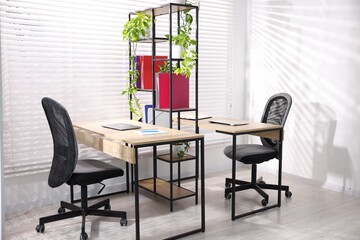Fototapeta premium Wooden desks with laptops, chairs, stationery, plants and shelving unit in office. Interior design